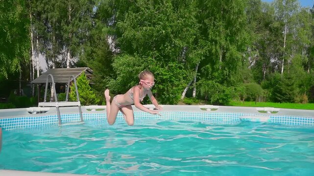 A joyful young girl makes a big splash as she jumps into a backyard frame pool on a hot sunny day. A perfect shot of summer vacation, family fun, and carefree childhood