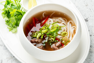 Vietnamese pho noodle soup in bowl with meat, chili, green onion, lime wedges, and cilantro. Traditional Asian cuisine served fresh and appetizing.