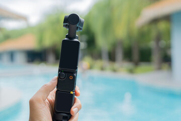 Action camera with three-axis suspension on woman hand over swimming pool