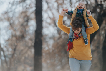 A cheerful woman carrying her happy child on shoulders while walking amidst a beautiful...