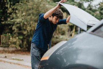 A man with curly hair is examining a car engine outdoors. He appears focused, suggesting an...
