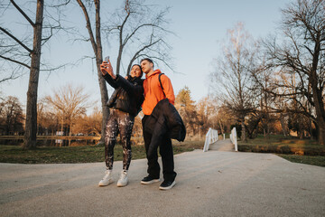 A young couple poses for a selfie in the park at golden hour as they enjoy the beautiful sunset...