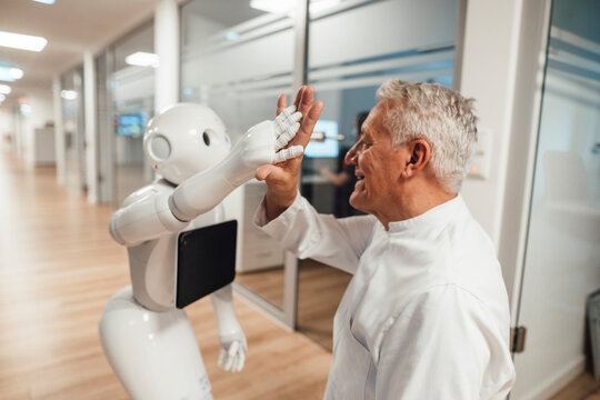 Medical professional giving robot high five in modern clinic