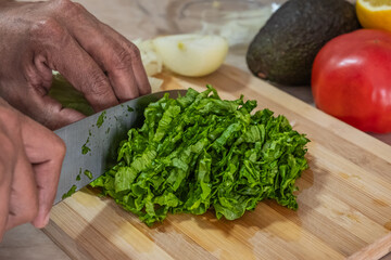 Cutting board and salad with green vegetables. Man preparing salad with lettuce, avocado and tomato