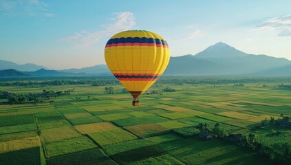 Obraz premium Yellow hot air balloon floats above lush rice paddies and mountains