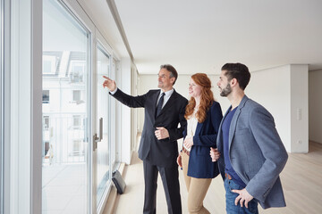 Businessman pointing at view to young couple from new apartment