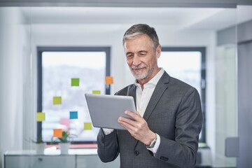 Smiling senior businessman working on tablet PC in office