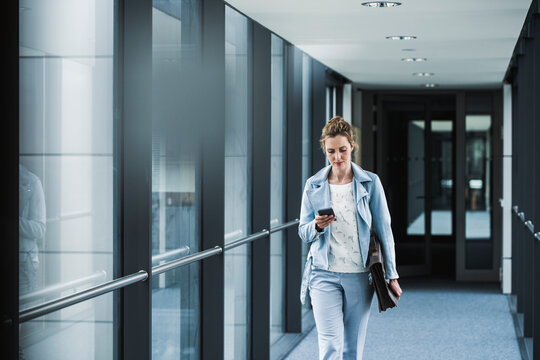 Businesswoman with cell phone walking in office passageway