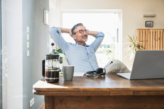 Freelancer with hands behind head sitting at desk in home office
