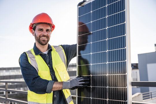Smiling engineer standing by solar panel at terrace