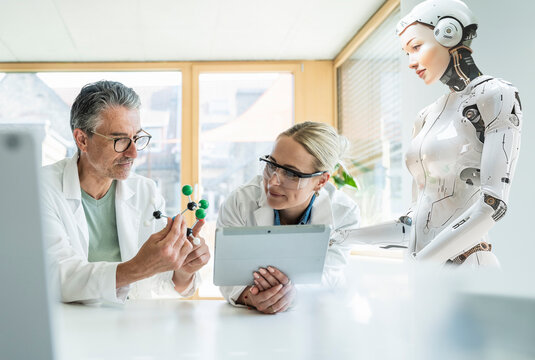 Scientists using tablet PC and examining atom model with robot in office