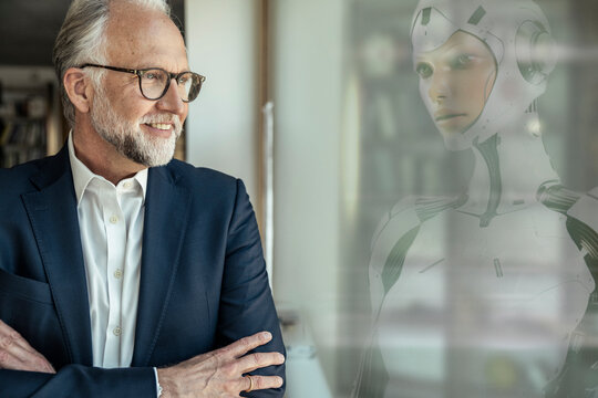 Smiling businessman looking at cyborg from window in office