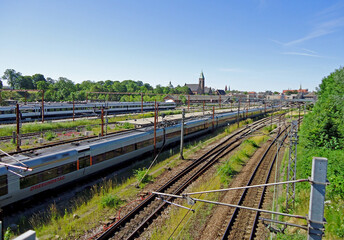 Obraz premium Railway station on a sunny day. A wide shot of a railway station on a clear, sunny day with trains waiting on multiple tracks and a cityscape in the background.