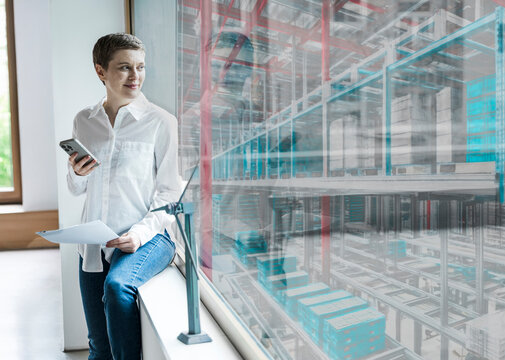 Manager with smartphone and documents smiling in modern industrial office