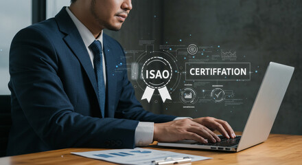 Man in suit typing on laptop with isao certification graphic overlay on screen and desk with reports