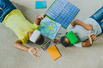 Siblings wearing virtual reality simulators and lying near solar energy school project on carpet