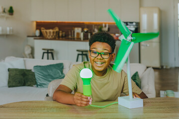 Happy boy powering light bulb through wind turbine model at home