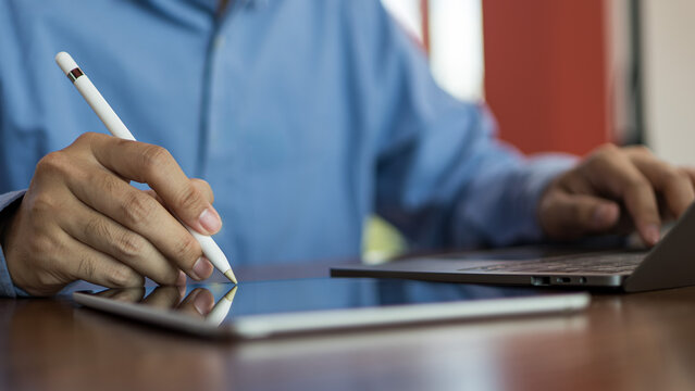 Man using stylus on tablet while working with laptop for digital work and creative task