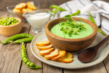 Green pea soup on a wooden table. Fresh pea soup bowl. Delicious healthy cream soup in a bowl with green peas and croutons. Healthy vegan puree. Copy space. Space for text.