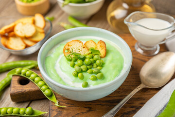 Green pea soup on a wooden table. Fresh pea soup bowl. Delicious healthy cream soup in a bowl with green peas and croutons. Healthy vegan puree. Copy space. Space for text.