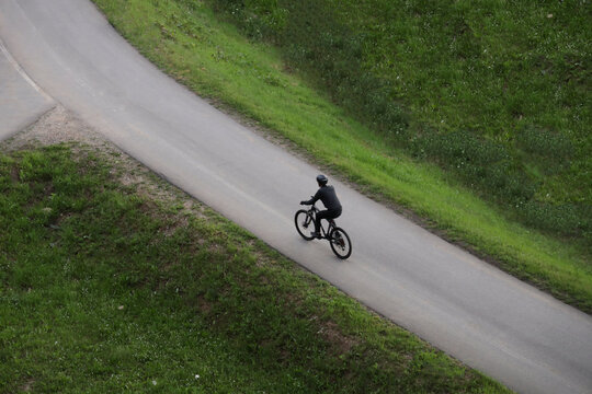 Aerial top view of one alone Cyclist with helmet riding on sporty cross bicycle on asphalt road grass background Man ride bike on an empty road with white lines. male wearing black helmet clothes - Powered by Adobe