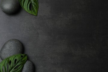 Top view of spa stones set for massage with green leaves on black concrete background with copy...