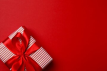 Elegant red wrapped gift box with ribbon placed on a color surface 