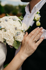 on the chest of the groom, dressed in a black jacket, to which a floral boutonniere is attached,...