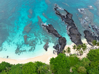 Tropical  Rolas Island on São Tomé aerial view with black volcanic rocks, white sand, turquoise water and lush green palm forest.