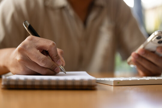 person writing notes in a notebook while holding a smartphone, concept for multitasking, productivity, planning, business organization, and creative work process.