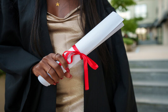 Close up of graduate holding diploma scroll outdoors in graduation robe