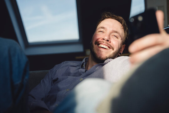 Smiling student relaxing at home in sunlight with smartphone - Powered by Adobe