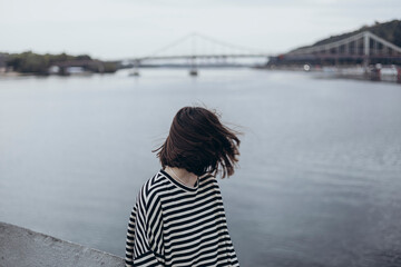 Elegant fashionable woman wearing striped long sleeve shirt near bridge.
