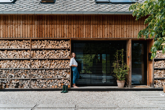Woman standing in front of eco friendly house with stacked firewood