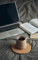 Cup of coffee, Bible book and laptop on gray bed in bedroom, cozy mood.