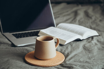 Cup of coffee, Bible book and laptop on gray bed in bedroom, cozy mood.