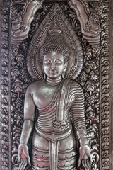 Chiang Mai, Thailand - July, 18, 2025 : Intricate metal carving of a standing Buddha on a richly...