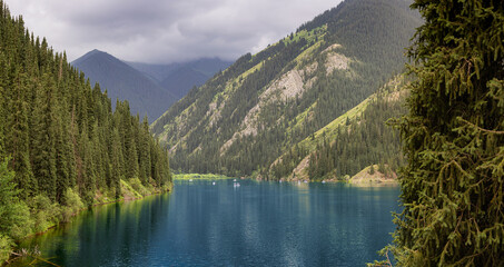 Picturesque Kolsai Lakes mirroring the beauty of Tian Shan mountains and evergreen forests under a cloudy sky