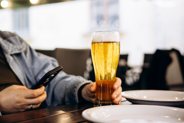 Man drinking beer from glass in cafe while using smartphone.