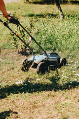 Photo of a person’s hands holding a lawn mower while cutting grass. The mower and green lawn are...