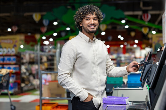 Man at a self-checkout terminal in a store, utilizing a smartphone for payment.