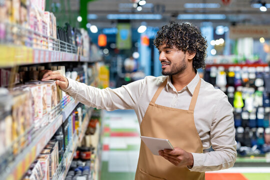 A grocery store employee stocks shelves while using a tablet. The image demonstrates modern retail management, customer service, and the daily responsibilities in a vibrant supermarket setting.