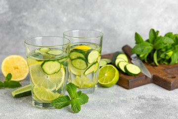 Cucumber water with lemon, lime and mint on a wooden table. Water infused with sliced ​​cucumber in a drinking glass. Tonic refreshing drink. Cucumber lemonade.Summer natural cooling drink.Copy space