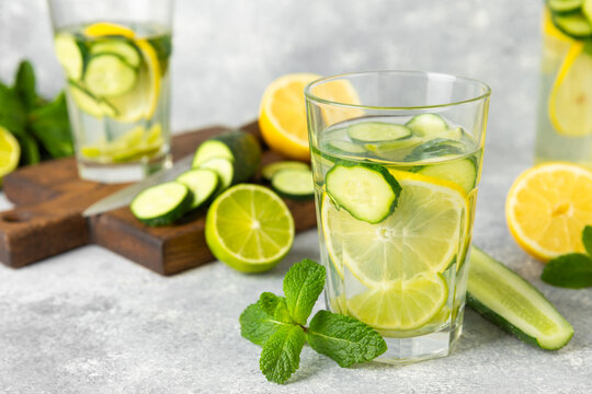 Cucumber water with lemon, lime and mint on a wooden table. Water infused with sliced ​​cucumber in a drinking glass. Tonic refreshing drink. Cucumber lemonade.Summer natural cooling drink.Copy space