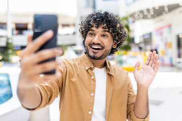 A cheerful young man with curly hair enjoying a moment while capturing a selfie indoors during the day.