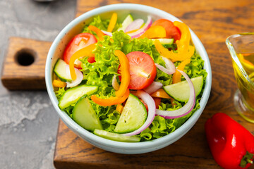Cucumber salad on a wooden background.Homemade salad with fresh vegetables, cucumber, tomato, sweet pepper and lettuce in a plate.Vegetarian spring salad.Vegetarian diet.Healthy eating.Space for text