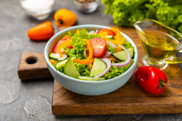 Cucumber salad on a wooden background.Homemade salad with fresh vegetables, cucumber, tomato, sweet pepper and lettuce in a plate.Vegetarian spring salad.Vegetarian diet.Healthy eating.Space for text