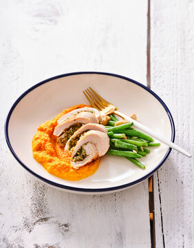 A delectable serving of garlic and herb stuffed chicken accompanied by creamy sweet potato mash and crisp green beans creates a delightful dinner plate. This dish combines rich flavors and textures