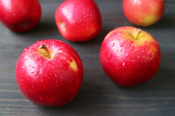 Closeup of red fresh ripe apples with water droplets scattered on black wooden table
