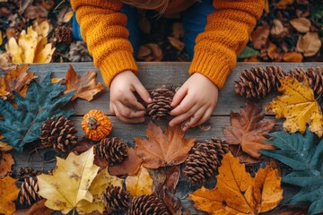 Child arranging pine cones and leaves during autumn on a wooden table